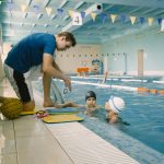 Two schoolgirl water polo players listening to teacher poolside.Have fun, play and splash in a blue swimming pool